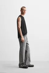 Pantalón de jean negro con efecto lavado, corte flare, cinco bolsillos, cierre frontal con cremallera y botón, y bajo con acabado irregular.