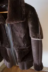 Campera gamulán marrón con cierre frontal, cuello solapa y bolsillos laterales.