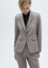 Blazer color gris topo, con cuello de pico con solapa y solapas con muesca. Tiene un bolsillo de ribete en la parte delantera, manga larga con puños abotonados, diseño recto, dos bolsillos de solapa en la parte delantera y cierre delantero de botón.