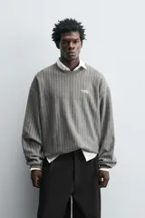 Sudadera gris con rayas verticales blancas, cuello redondo, manga larga y bordado con texto en el pecho.