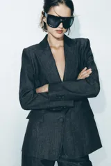 Blazer gris oscuro con cuello solapa, manga larga, bolsillos con solapa en el delantero y cierre frontal con dos botones forrados.