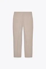 Pantalón de vestir color beige, de tiro bajo, corte recto y largo cropped. Cuenta con bolsillos laterales y traseros, cierre frontal con cremallera y gancho metálico, y abertura lateral en el bajo.