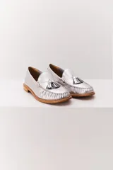 Mocasín de cuero color marrón claro, con detalle de flecos y borlas en la parte delantera. Diseñado en Uruguay y fabricado en Brasil.