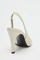 Zapato de tacón en piel color beige con abertura lateral, punta fina y cierre con tira ajustable. Tacón alto fino de 10,5 cm.