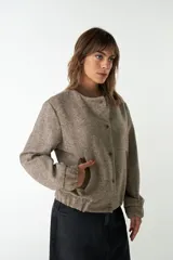 Campera estilo bomber de cuello redondo, color beige jaspeado, con cierre frontal de broches y bolsillos delanteros con ribete marrón.