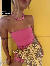 Falda pareo corta con estampado tropical en tonos amarillo y marrón, con motivos de palmeras y peces. Se anuda en la cintura y tiene un corte asimétrico.
