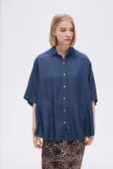Camisa celeste de manga corta, corte holgado, con cuello camisero y cierre frontal con botones.