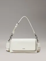 Cartera de hombro rectangular color blanco, con solapa frontal y logo metálico de Calvin Klein. Cuenta con dos correas desmontables: una fina ajustable y una ancha de tela con inscripción.