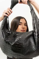 Bolso tipo hobo de cuero color beige, con asa anudada al hombro y cierre superior con cremallera.