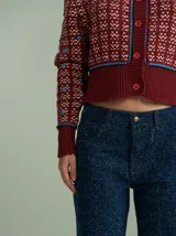 Cardigan de punto color borgoña con diseño geométrico en blanco y detalles en azul. Tiene cuello redondo, cierre frontal con botones rojos y mangas largas con puños acanalados.