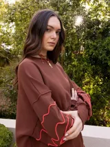 Buzo marrón de corte holgado, con cuello redondo y mangas largas. Presenta bordados florales en color naranja en los puños.