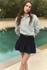 Remera gris con cuello polo, de corte cropped y manga larga. Presenta apliques de strass y bordado con el número 85 en el pecho.