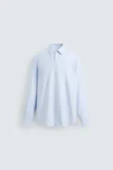 Camisa celeste de algodón con corte regular fit, cuello italiano, manga larga con puños abotonados y cierre frontal con botones.