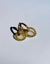 Par de aros colgantes con argollas doradas y dijes circulares de resina transparente con incrustaciones de strass de colores. El dije mide aproximadamente 1.5cm de diámetro.