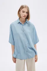 Camisa celeste de manga corta, corte holgado, con cuello camisero y cierre frontal con botones.
