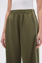 Pantalón deportivo negro de corte ancho y tiro alto, con cintura elástica y cordón ajustable. Presenta una raya blanca vertical a cada lado.