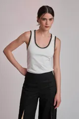 Remera negra ajustada al cuerpo, tipo musculosa, con escote redondo y ribetes en blanco con apliques de perlas en el contorno del cuello y las sisas.