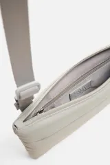 Bandolera negra fabricada en tejido técnico con correa ajustable. Tiene un compartimento principal con cierre de cremallera, un bolsillo interior con cremallera y un bolsillo frontal con cremallera y detalle de arnés.
