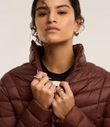 Campera puffer ultraligera color marrón, confeccionada en poliamida acolchada, con cuello alto y cierre por cremallera. Incluye bolsita con cordón.