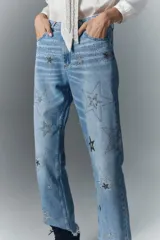 Pantalón de jean de tiro alto, denim azul rígido con lavado localizado, apliques de brillos, pierna recta y ruedo desflecado.