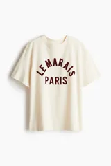 Remera color crema de corte holgado, con cuello redondo y estampado frontal con la frase "Le Marais Paris" en color borgoña.