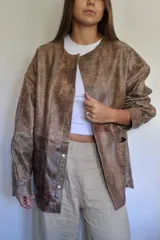 Campera de cuero color marrón con cuello redondo, cierre frontal con botones a presión, bolsillos laterales y corte holgado.