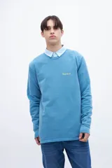 Buzo celeste de felpa liviana con cuello redondo, puños en mangas y bajo holgado. Tiene un bordado pequeño en el pecho con la inscripción "Uniform St.".