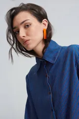 Camisa azul con rayas verticales color naranja, de corte holgado, mangas largas con pinzas laterales y puños anchos. Cuello clásico de gran tamaño.