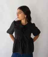 Blusa negra de popelina de algodón con corte peplum, mangas abullonadas y lazo en el cuello.