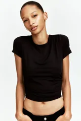 Remera cropped negra de punto elástico, entallada con costuras fruncidas en un hombro y a ambos lados de la cintura para crear un leve efecto drapeado.