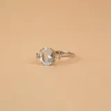 Anillo solitario de oro blanco 18k con aguamarina central ovalada y brillantes laterales engarzados en 4 puntas. El ancho de la banda es de 2,4 mm.
