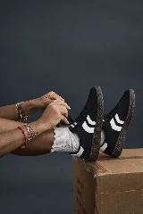 Championes deportivos Hummel modelo Gazelle, color negro con franjas laterales blancas y suela de goma marrón. Se usan con medias blancas de caña corta con borde ondulado.