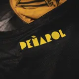 Musculosa deportiva negra con detalles en amarillo, escudo del Club Atlético Peñarol y logo de Puma.