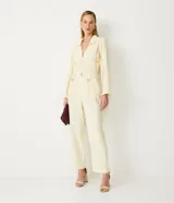 Pantalón recto color crema con cinturilla diferenciada, botones decorativos, pliegues delanteros y sin estampado.