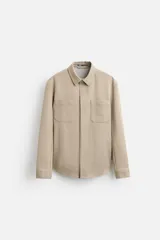 Sobrecamisa color beige de tejido con elasticidad, cuello solapa, manga larga con puño abotonado, bolsillos de plastrón en el pecho y cierre frontal con botones a presión.