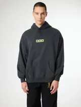 Buzo hoodie gris oscuro con corte boxy y estampado frontal central con tres cruces amarillas dentro de cuadrados.