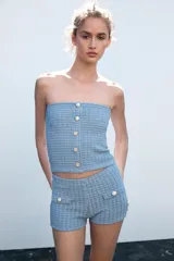 Shorts de tejido con textura color celeste, de tiro alto y cintura elástica. Presenta falsos bolsillos con solapa y botón metálico en el delantero.