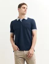 Chomba de piqué azul marino con cuello y mangas en gris. Tiene bolsillo en el pecho y tapeta con botones.