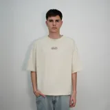 Remera color beige de corte oversize con estampado en la espalda que dice "Secret Company Venelo" y una cita bíblica.