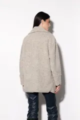 Cardigan de paño color beige, estilo chaqueta, con cuello esmoquin, corte amplio y bolsillos laterales.