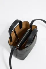 Bolso mini de piel vacuna color negro, con estructura blanda y formato vertical. Tiene doble asa corta, correa larga regulable, cierre con cinta, logo metálico BIMBA Y LOLA, acabados metálicos, bolsillo interior con cierre de cremallera e interior con logo grabado.