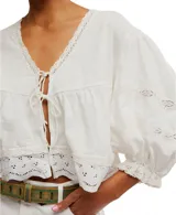 Blusa blanca de algodón con escote en V, mangas globo 3/4 con detalles de encaje y puños elásticos. Presenta lazos en el frente para atar.