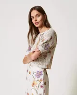 Top de tejido calado color crema con estampado floral en tonos lila, naranja y verde. Tiene cuello redondo y mangas cortas.