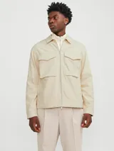 Chaqueta color crema, de manga larga, con cuello camisero y cierre frontal con cremallera metálica. Tiene dos bolsillos de parche con solapa en el pecho.