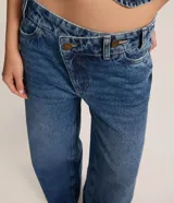 Pantalón de jeans azul de corte wide leg, tiro medio, con cintura de diseño traspasado y cierre tradicional.