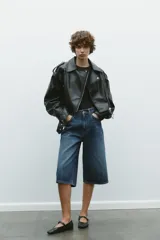 Cazadora biker corta de cuero sintético negro, con cuello solapa, trabillas en los hombros, bolsillos delanteros con cremallera, cinturón con hebilla metálica y cierre frontal con cremallera.