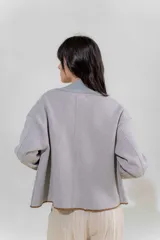 Chaqueta de punto color crudo con solapa ancha acanalada terminada con cadenetas en contraste negro. Tiene calce relajado, hombros caídos, largo a la cadera y manga larga.