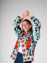 Chaqueta corta de color celeste con bordados florales en tonos rojos, naranjas, azules y negros.