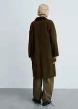 Anorak largo color verde militar con cuello camisero marrón de pana, cierre frontal con botones, bolsillos laterales y forro interior.