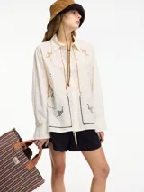 Camisa color crema con bordados y calados en el frente y la espalda, cuello camisero, botones frontales y mangas largas con puños abotonados.